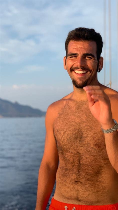 A Man With No Shirt On Standing In Front Of The Water Smiling At The Camera
