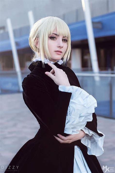 A Woman With Blonde Hair Wearing A Black Coat And White Dress Posing