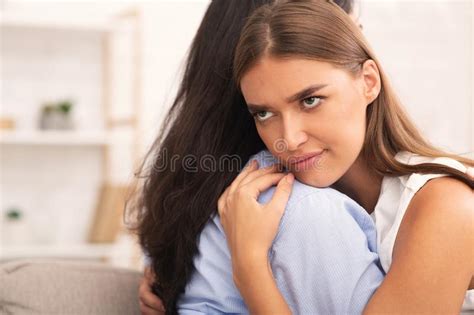 Girl Rolling Eyes Embracing Crying Friend Sitting On Sofa Stock Image