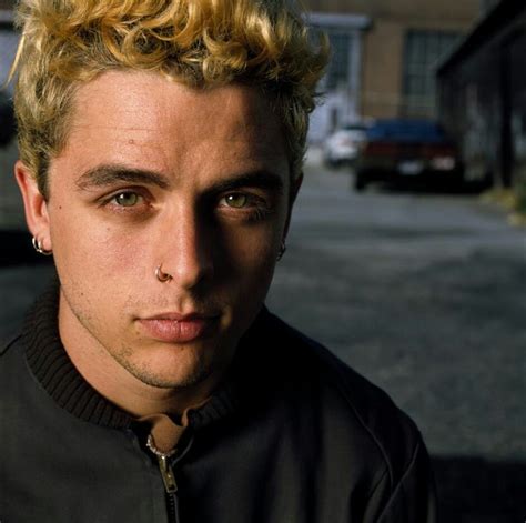A Man With Blonde Hair Wearing A Black Jacket And Looking At The Camera