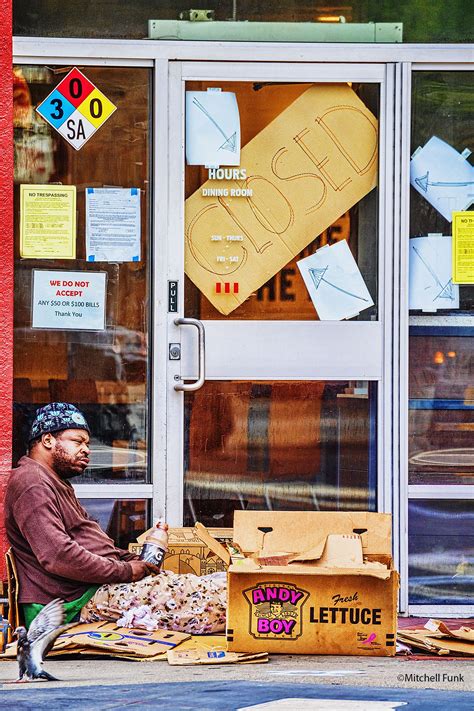 Homeless Man Sitting On Sidewalk In Front Of Closed Store In The