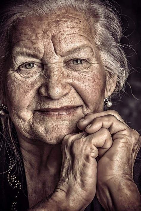 An Old Woman With Wrinkles On Her Face And Hands Looking At The Camera