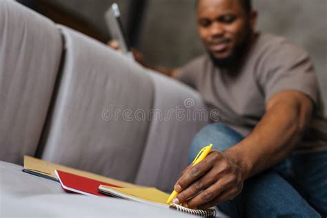Black Unshaven Man Using Tablet Computer While Writing Down Notes Stock