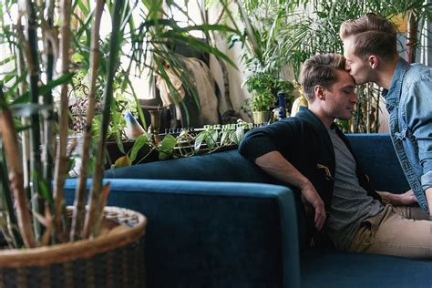 Gay Man Kissing On Boyfriend S Forehead Against Potted Plants At Home