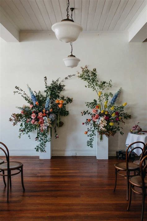 two vases filled with flowers sitting on top of a wooden floor next to chairs