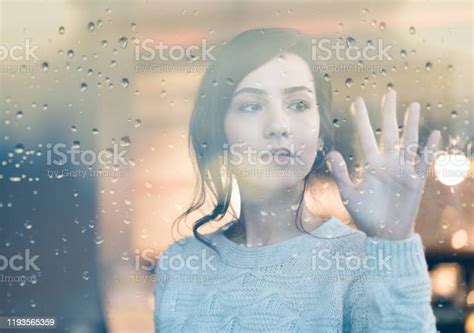 Sad Young Cute Woman Looking Through Window On Rainy Day Stock Photo