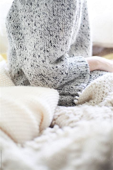 Young Woman Sitting On Bed With Cozy Sweater By Treasures And Travels