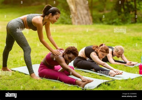 Young Female Yoga Instructor Teaching Group Of Sporty Women To Do Asanas Correctly Outside