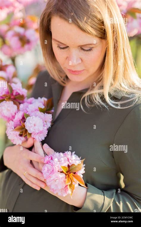 freckled blonde pregnant woman in the park at spring with sakura trees shallow depth of field