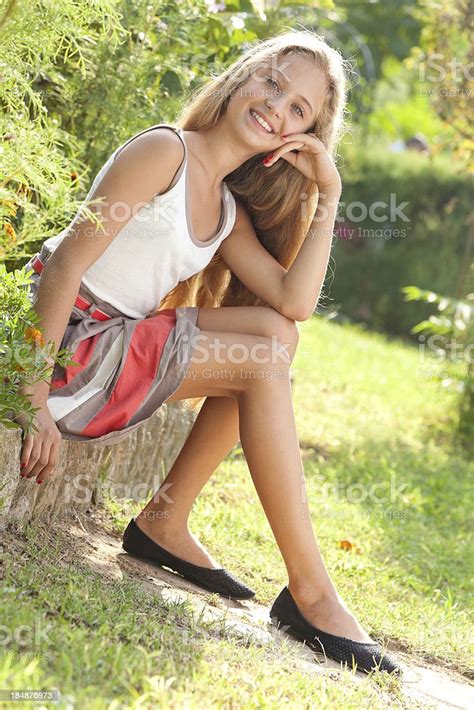 Attractive Teenage Girl Sitting Outdoors In Green Park Posing Smiling