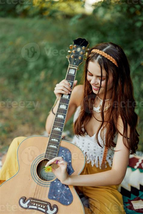 Lycklig hippie kvinna med en gitarr avkopplande i natur Sammanträde på