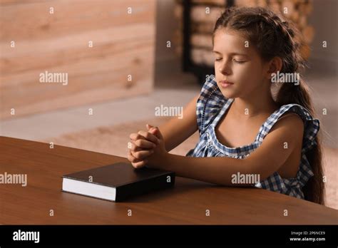 Cute Little Girl Praying Over Bible At Table In Room Stock Photo Alamy