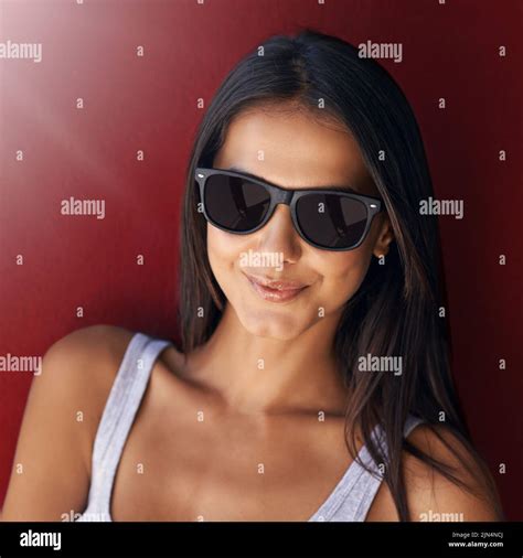 Cool Confident And Beautiful Woman Wearing Sunglasses And Smiling Against A Red Wall With Lens