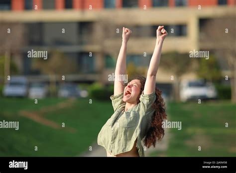 Excited Woman Raising Arms Celebrating Success In A Park Stock Photo