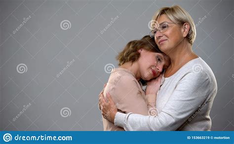 Mature Woman Hugging Adult Daughter On Grey Background Motherhood