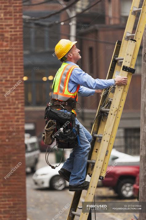 Cable Lineman Climbing Up A Ladder On City Building — Tool Belt On The