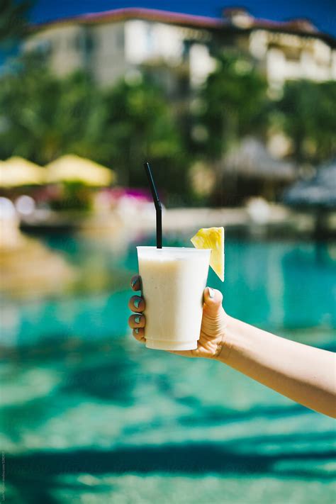 Woman Holding Out Pina Colada Drink At Resort Swimming Pool By