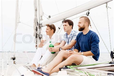 Happy Friends Sitting Together On A Deck Of A Yacht And Drinking An