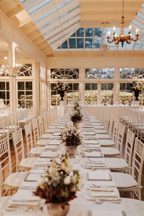 A Long Table With White Chairs And Place Settings Is Set Up For A