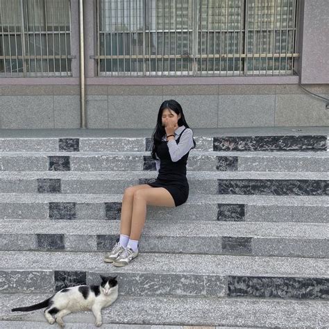 a woman sitting on steps next to a black and white cat with its tail up