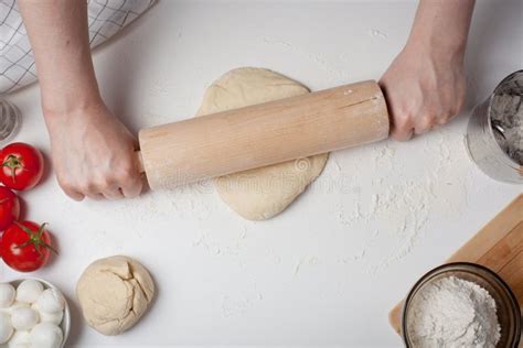 Female Hand Rolled Pizza Dough With A Rolling Pin On A White Table