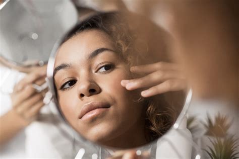 Young Afro Woman Looking In Mirror Integrated Dermatology Of Reston