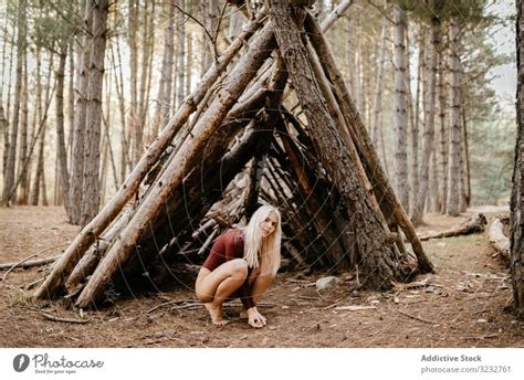 Barefoot Woman Squatting Beside Primitive Shelter In Woods A Royalty
