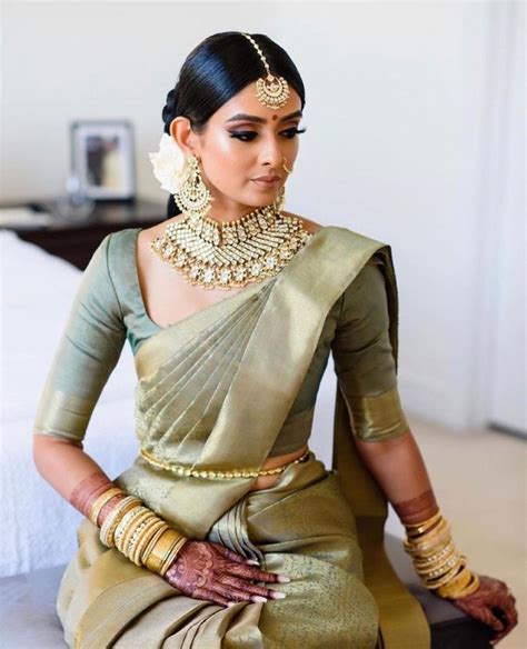 A Woman Sitting On Top Of A Bed Wearing A Green And Gold Sari Dress
