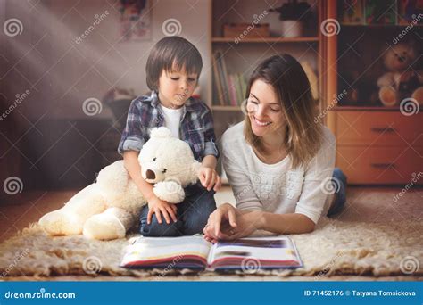 Potomstwa Matkują Czytają Książkę Jej Dziecko Chłopiec W żywym Pokoju O Zdjęcie Stock Obraz