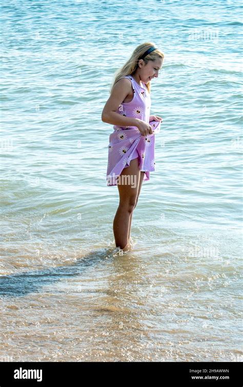 Young Girl Hikes Up Her Dress To Keep It Out Of The Water As She Walks