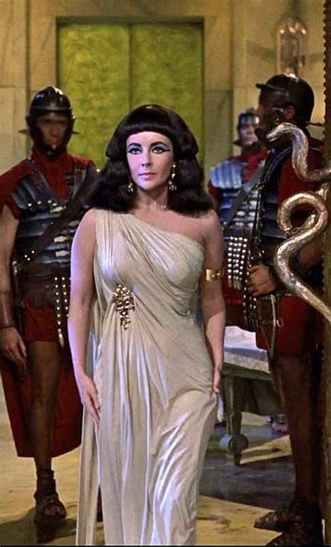A Woman In A White Dress Standing Next To Two Men Wearing Roman Garb And Helmets