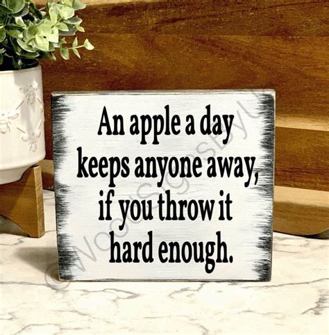 A Wooden Sign That Says An Apple A Day Keeps Anyone Away If You Throw It Hard Enough