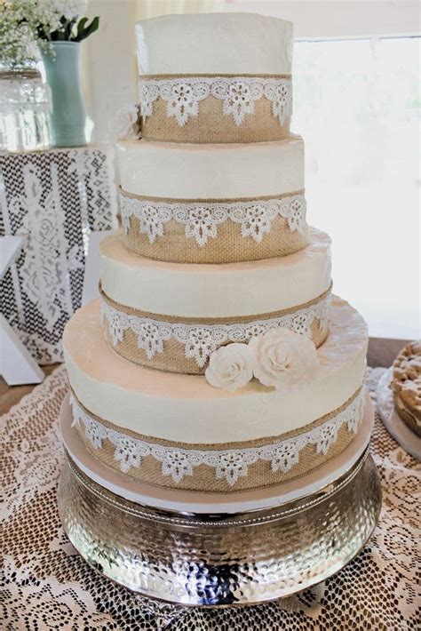 A Three Tiered Wedding Cake With Lace And Flowers On The Top Is Sitting
