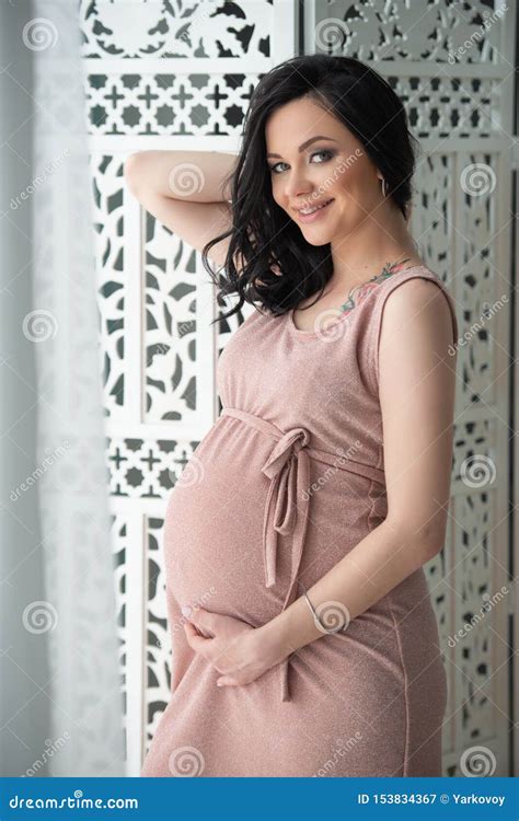 women`s health and pregnancy a beautiful pregnant woman in a tender pink dress is standing near