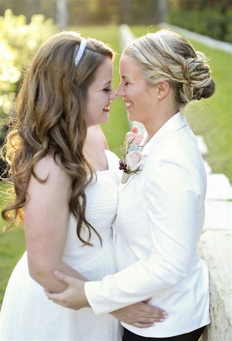 Two Women In White Dresses Standing Next To Each Other On A Stone Wall And Looking At Each Other