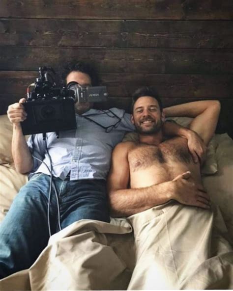 Two Men Laying In Bed And One Is Holding A Camera