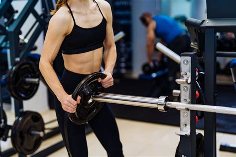 Premium Photo Professional Sport Fitness Woman Putting Weight Disk To Barbell In Gym