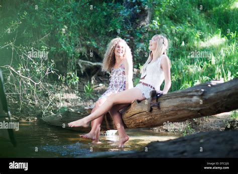 Two Teenage Girls Sitting On Tree In Woodland Stream Stock Photo