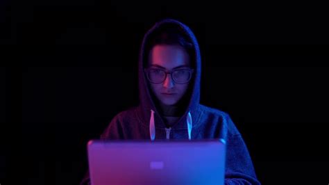 Young Woman In A Hood With A Laptop Hacker Makes A Hack Through A