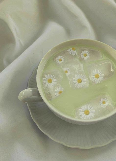 A Cup Filled With Water And Daisies Sitting On Top Of A White Table Cloth