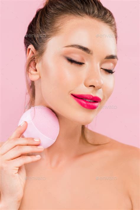 Pleased Naked Beautiful Woman With Pink Lips Using Facial Cleansing Brush With Closed Eyes