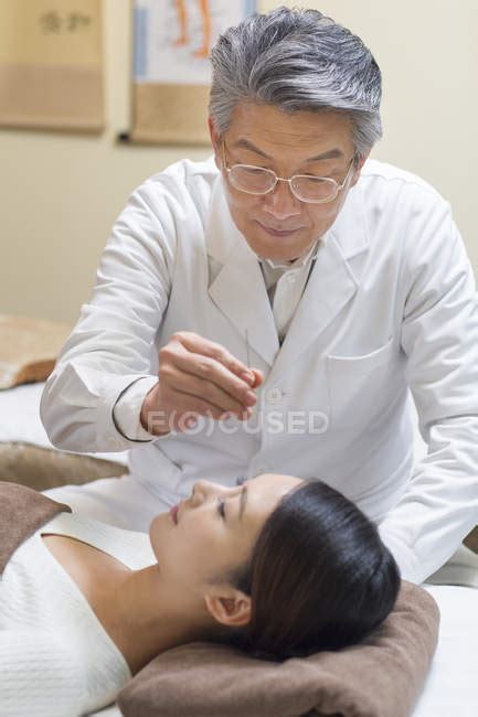 Senior Doctor Performing Acupuncture Treatment On Female Face
