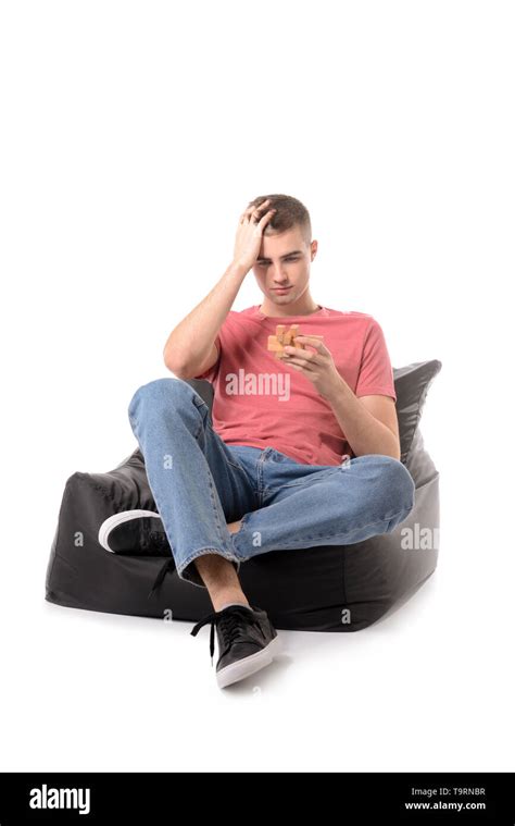 Young Man With Brain Teaser Sitting On Frameless Armchair Against White