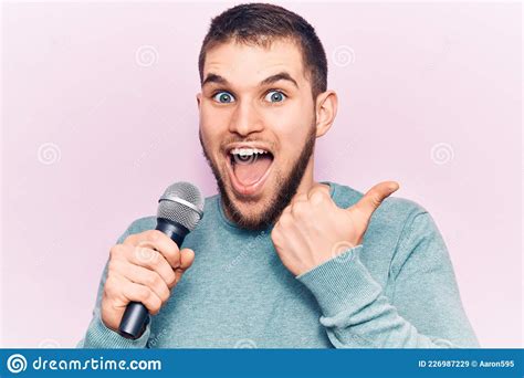 Young Handsome Man Singing Song Using Microphone Pointing Thumb Up To
