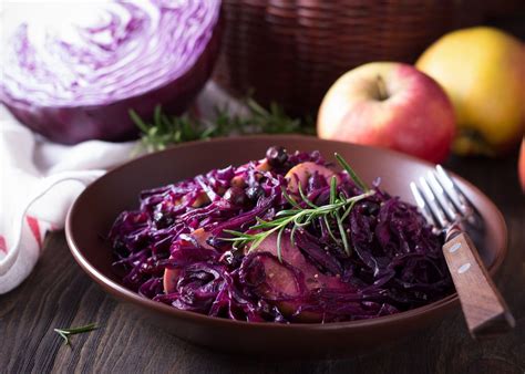 A brown bowl filled with red cabbage and apples next to a knife and