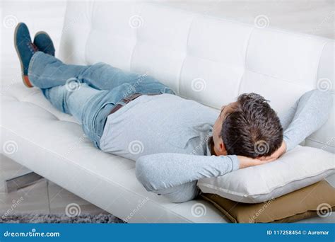 Man Laying On Sofa Holding Smartphone And Remote Control Royalty Free