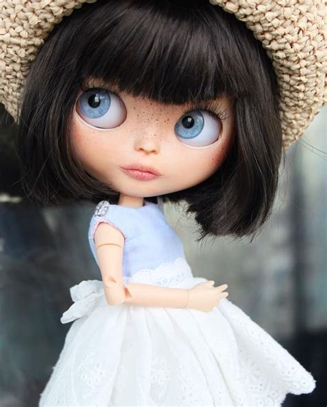 A Close Up Of A Doll Wearing A Dress And A Knitted Hat With Big Blue Eyes