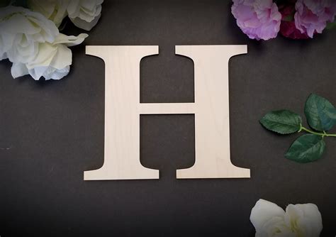 The Letter H Is Made Out Of Wood And Sits Next To Flowers On A Black