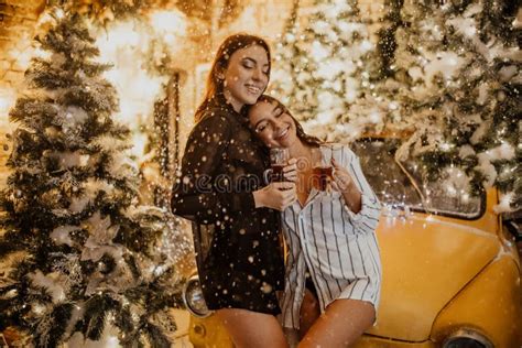 Lesbian Couple Hugs Against Background Of Christmas Decorations And Retro Car Stock Image