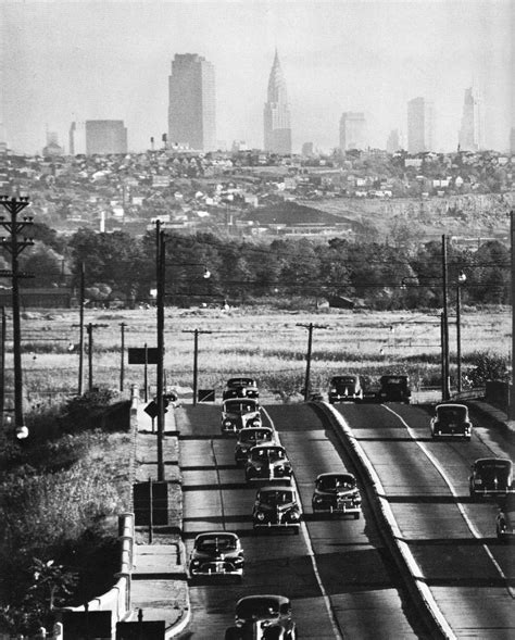 an old black and white photo of cars driving down the road in front of a city